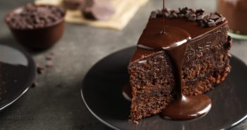 Pouring chocolate sauce onto delicious fresh cake on grey table, closeup