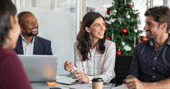 Group of happy business people in meeting during christmas holiday. Smiling businessman and businesswoman discussing new project strategy during xmas time. Successful multiethnic business partners in a conversation in modern office.