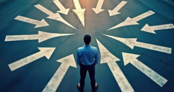 Man stands at crossroads. Many arrows point in different directions. Seems indecisive confused about options. Choices, decisions key concepts. Considering different paths, possibilities in life
