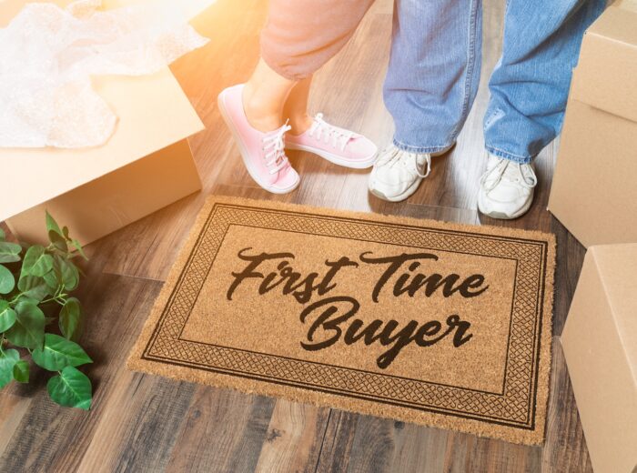 Man and Woman Unpacking Near Our First Time Buyer Welcome Mat, Moving Boxes and Plant.