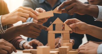 A poignant symbol of community building, cooperation, and inclusion. Each distinct hand represents a unique individual, and their act of building a home together symbolizes the collective effort to create a safe, supportive, and inclusive space for all.