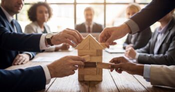 Business team building house model from wooden blocks in meeting, concept of teamwork, real estate planning, mortgage, insurance and investment strategy.